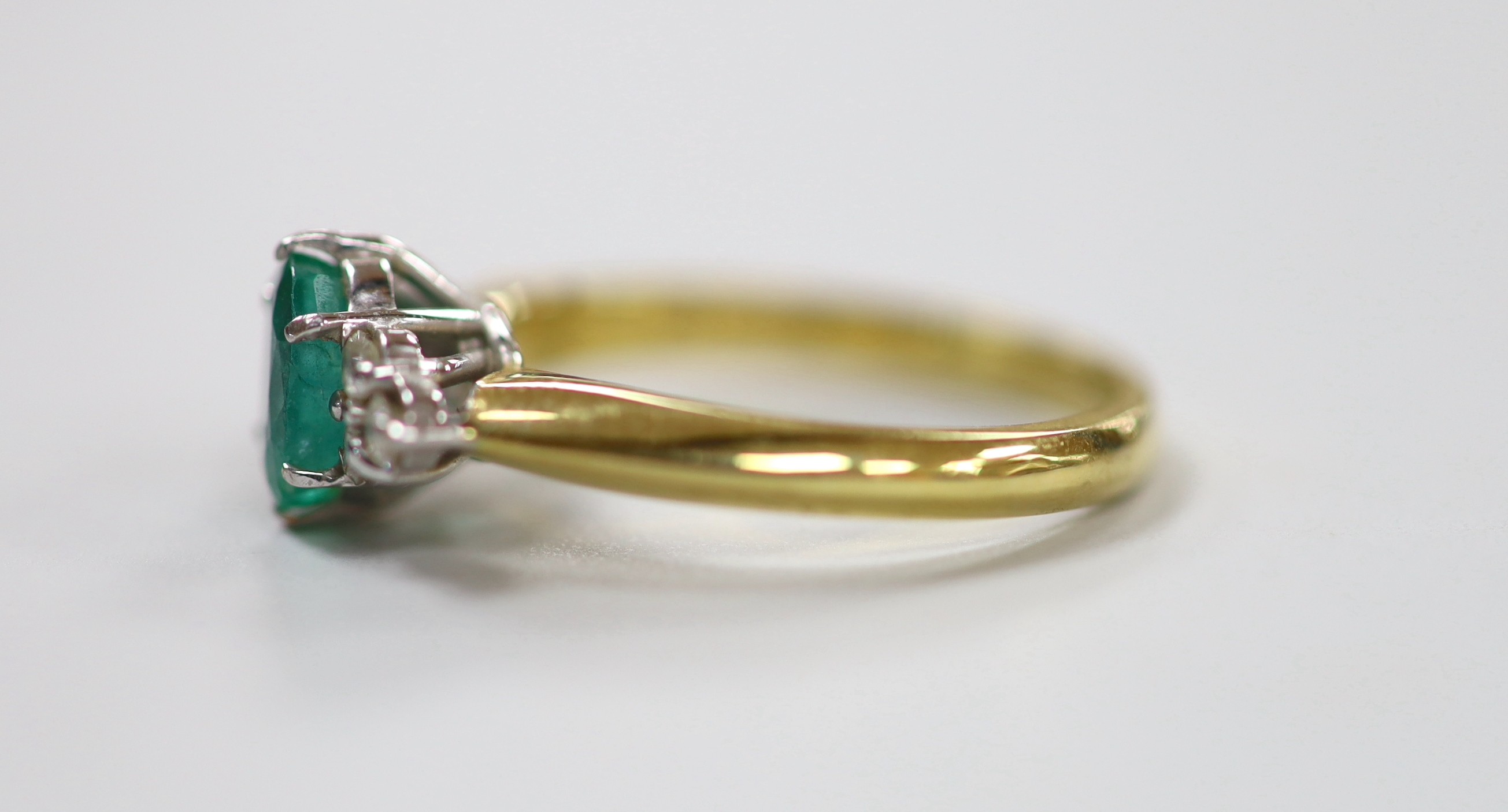 A modern 18ct gold and single stone oval cut emerald set ring, with six stone diamond chip set shoulders, size N/O, gross weight 4.8 grams.